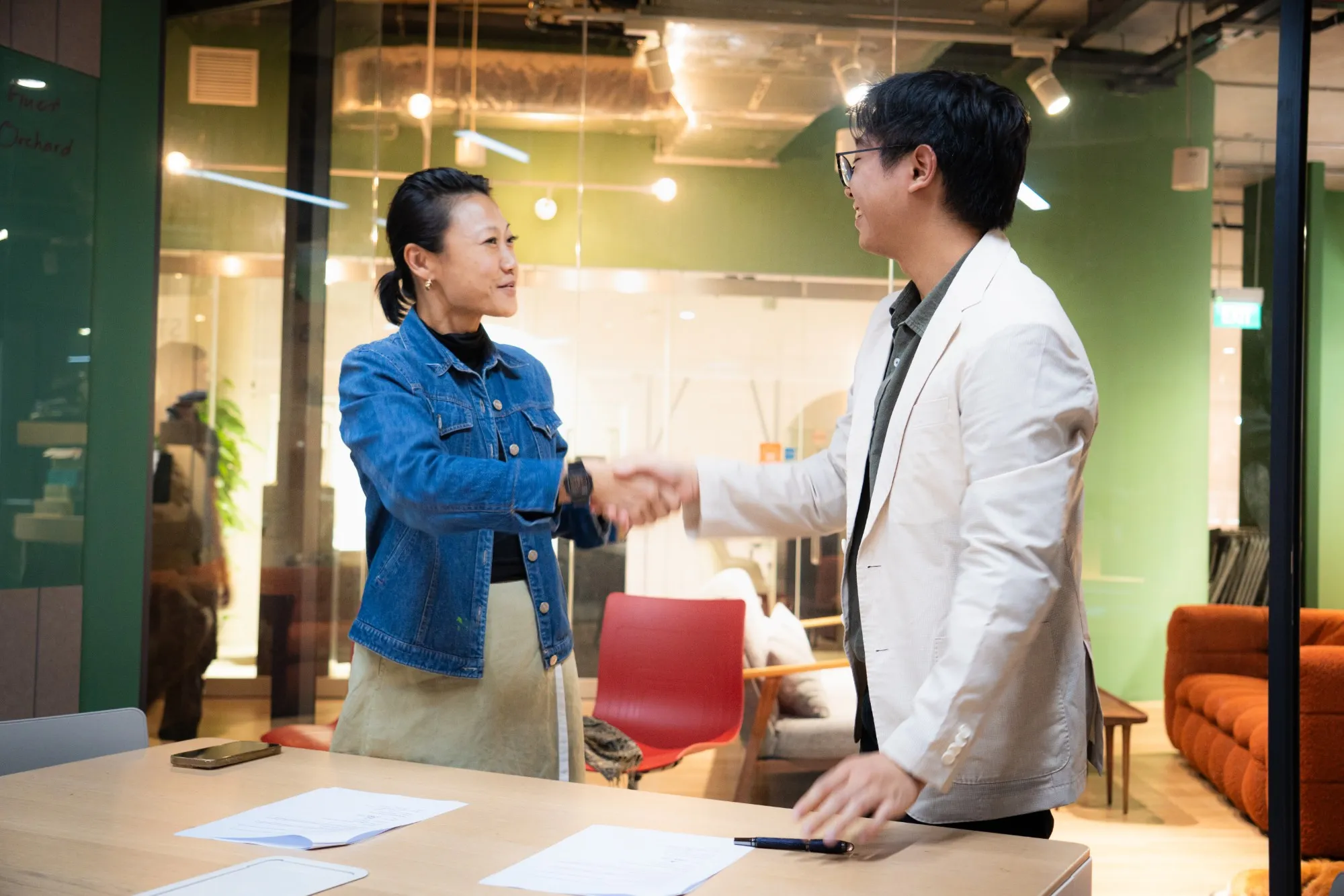 Benedict shaking hands with a woman across a meeting table with signed documents on it.